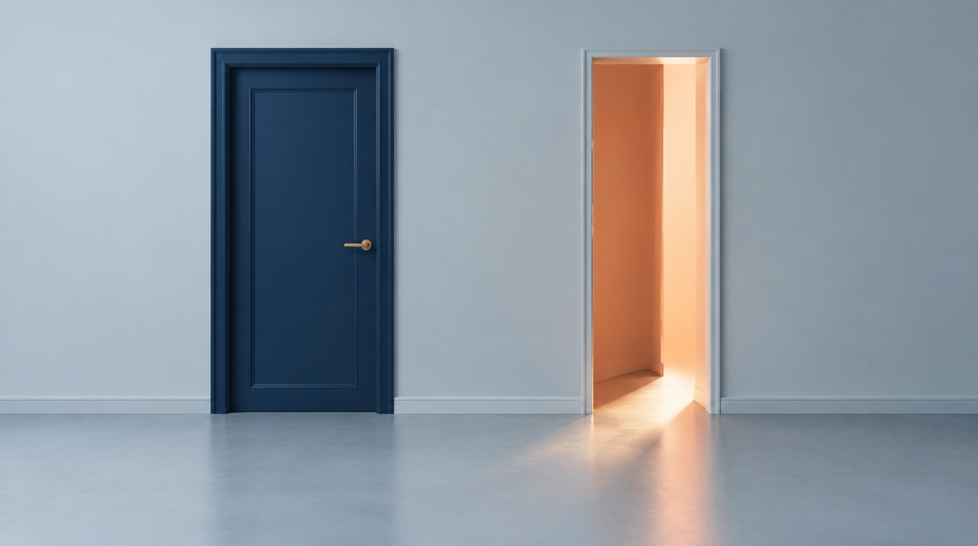 A closed navy door with a brass handle set into a pale wall, and beside it an open doorway with warm light spilling through onto the floor